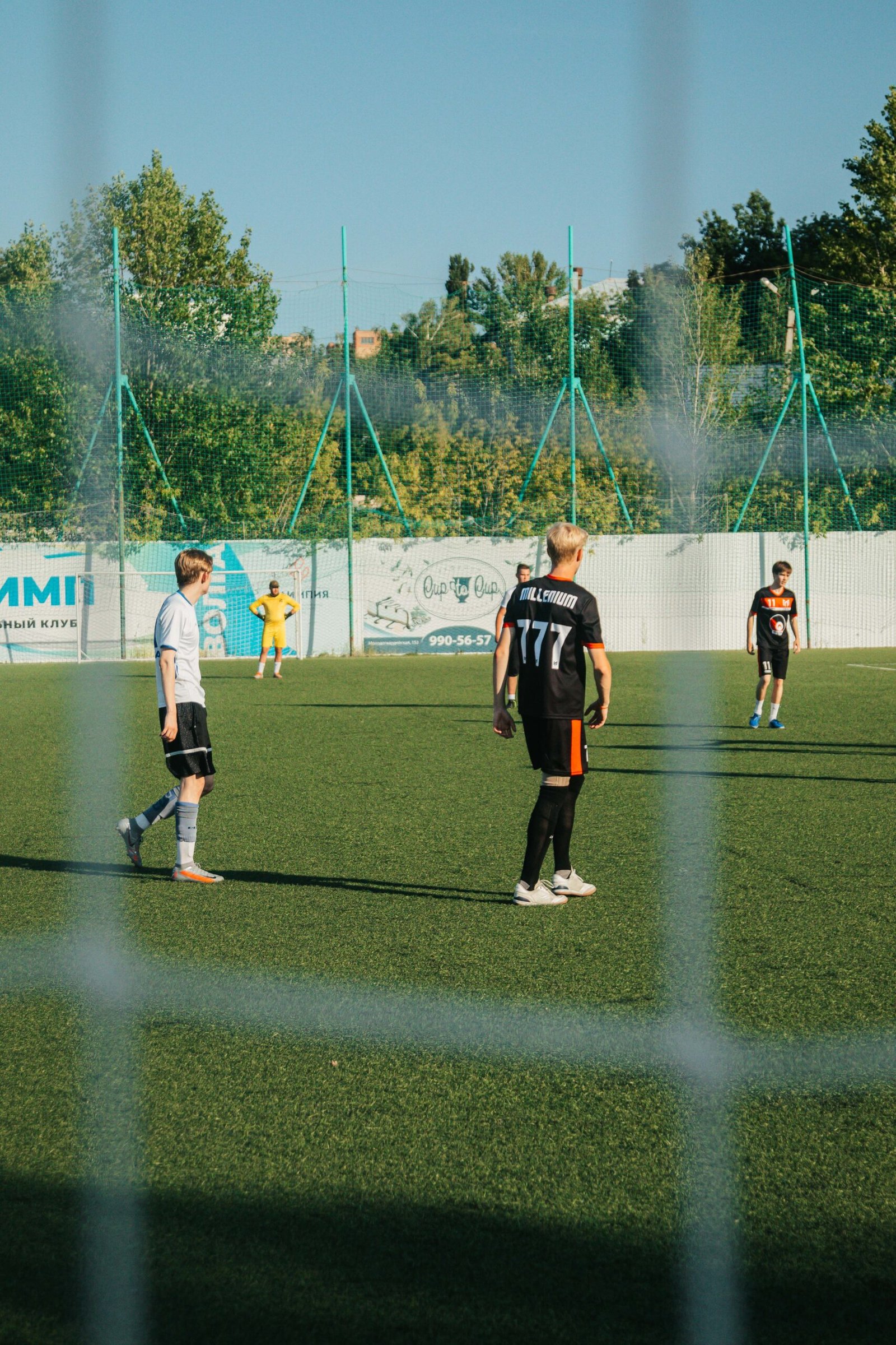 Soccer game on a sunny day with young men on the field, captured beyond the net.