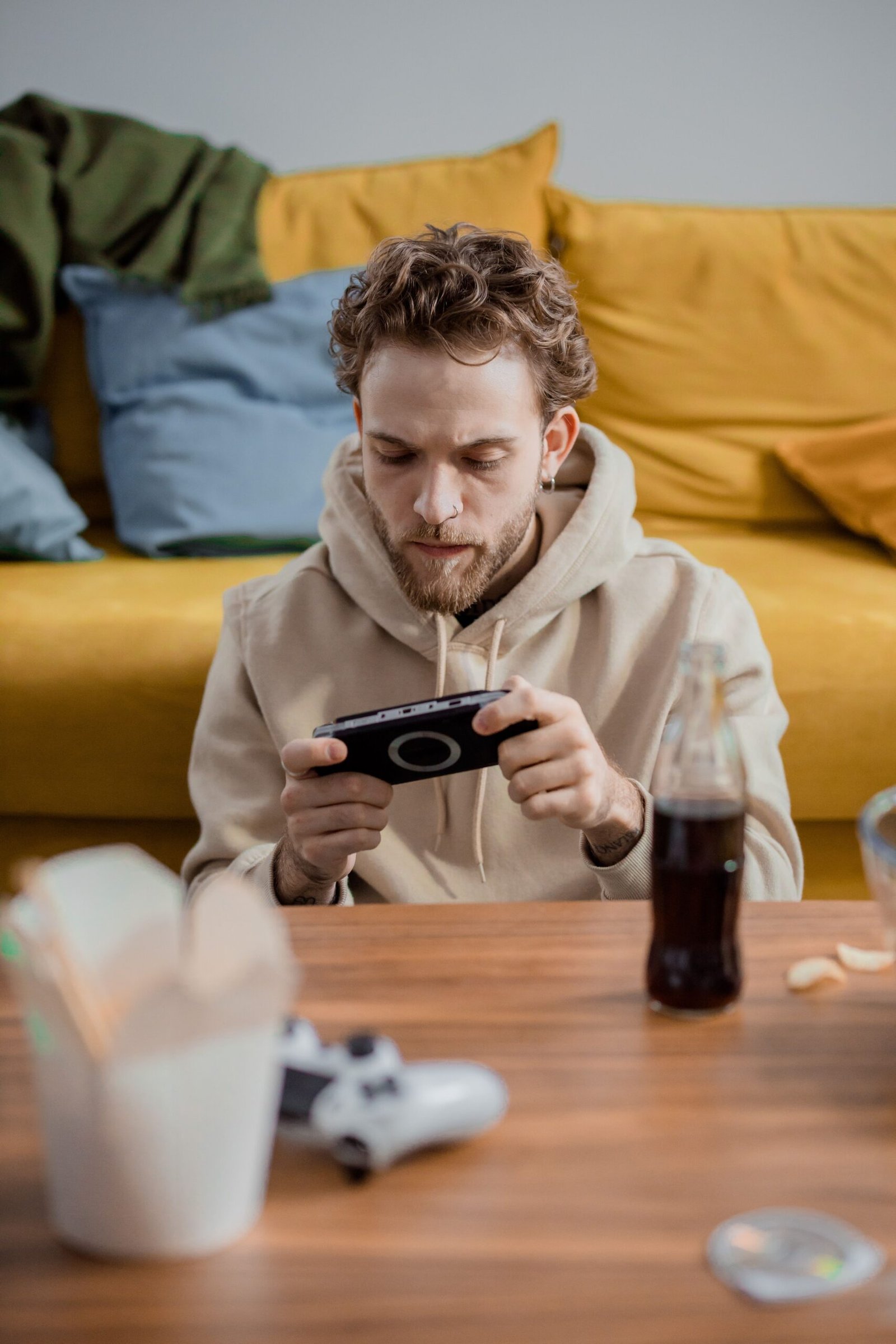 Young man focused on gaming while sitting indoors with a portable console and snacks.